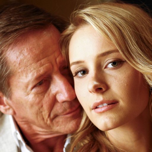 Young, blonde woman being kissed in an intimate way by a much older man